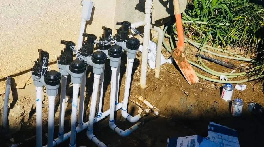 Multiple black and white PVC irrigation zone valves installed in organized rows with underground piping